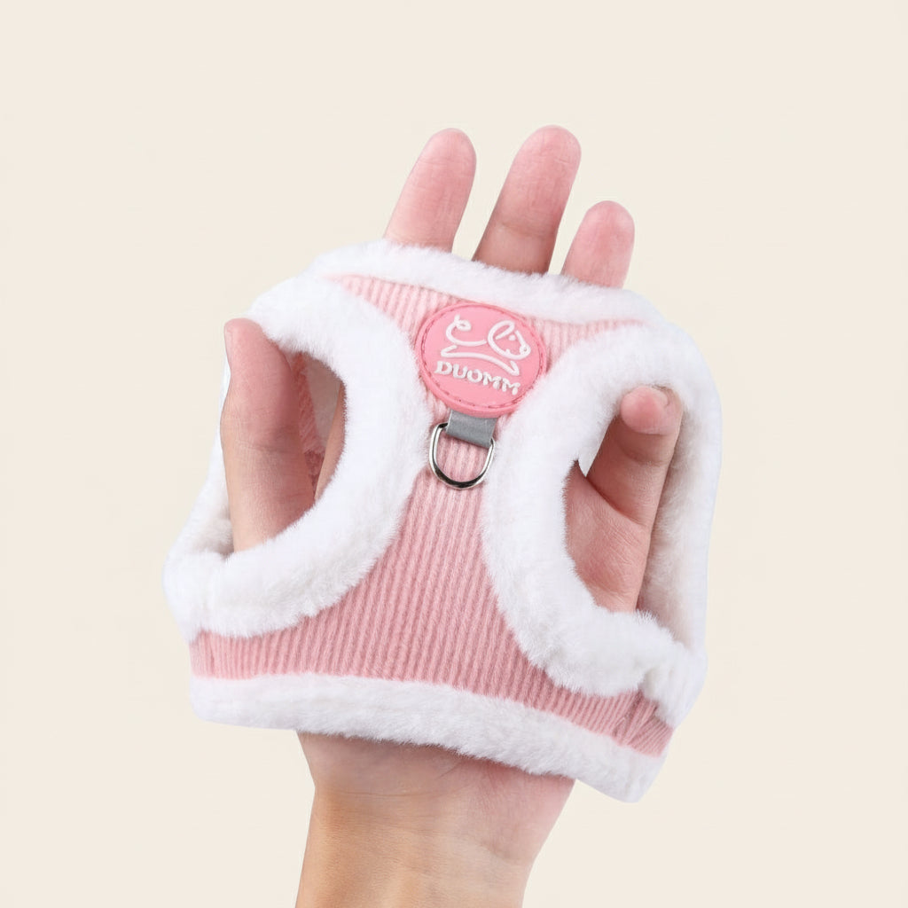 Nærbillede af lyserødt plysforet katteharnes holdt i en hånd for at vise størrelse, tykkelse og den bløde tekstur af fløjlsmaterialet.