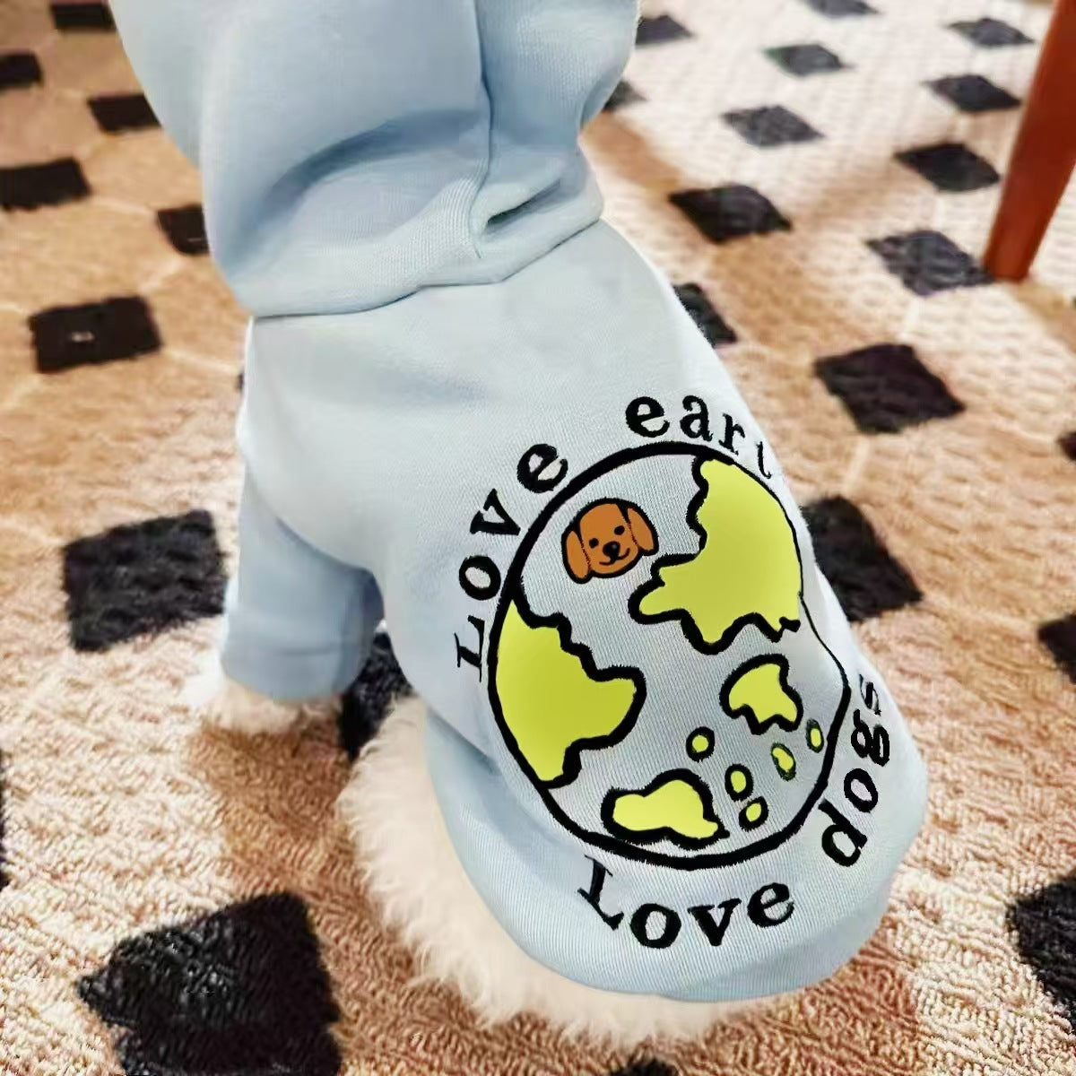 Billede af hund iført den blå "Love Earth Love Dogs" hættetrøje, siddende i en lys, minimalistisk dansk stue.