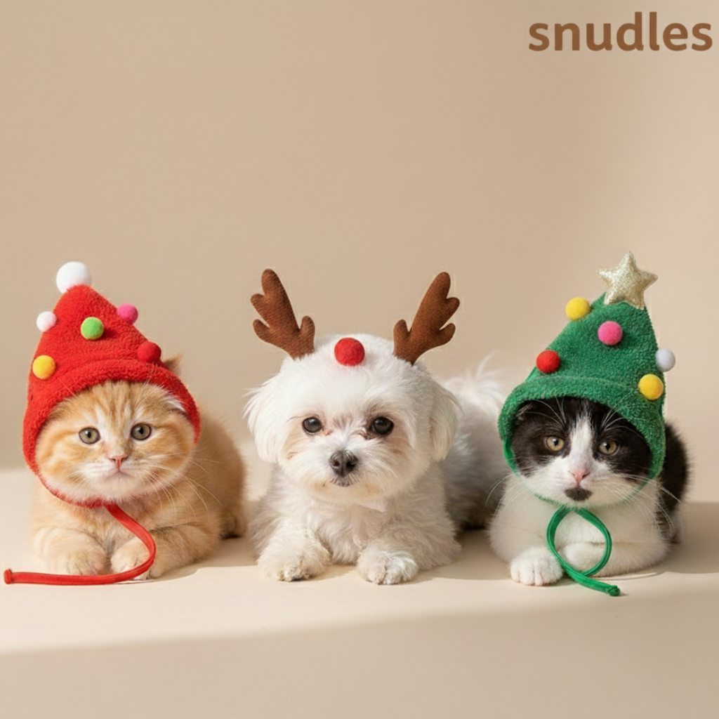 To fluffy killinger og en lille hvid hund iført unikke julehatte: en rød pomponhat, et rensdyrgevir pandebånd og en grøn juletræshat. Perfekt kæledyrs julekostume eller gaveidé. 'snudles' logo øverst til højre på lys beige baggrund.