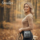 En attraktiv dansk kvinde med bølget lyst hår smiler, mens hun går tur med sin golden retriever gennem en stemningsfuld efterårsskov. Hun bærer en stilfuld grå godbidstaske komfortabelt om hoften og holder en foldet hundesnor i hånden. De varme, gyldne blade på træer og stier skaber en fredfyldt og indbydende atmosfære